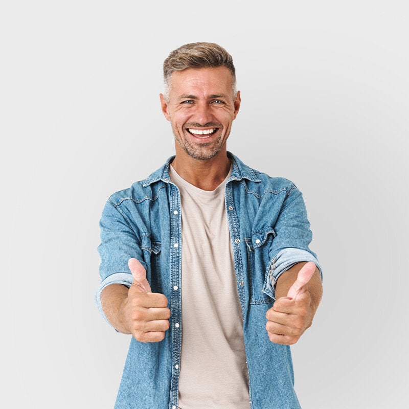 En glad man står och gör tummen upp med båda händerna och har en jeans jacka på sig